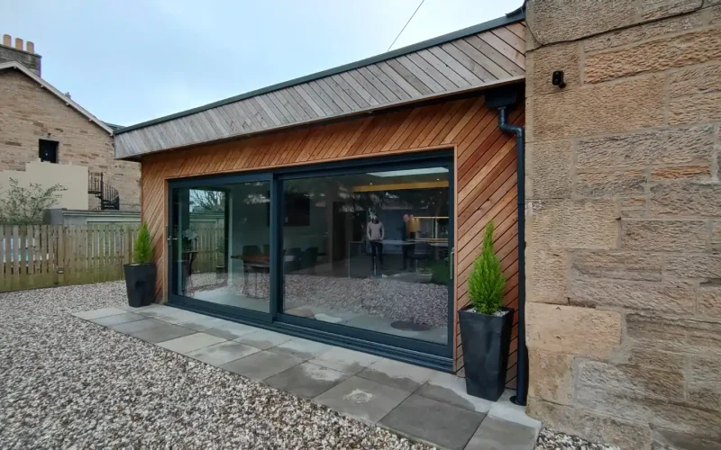 Stylish garden room with large glass sliding doors and timber cladding, perfect for outdoor living and home office space.