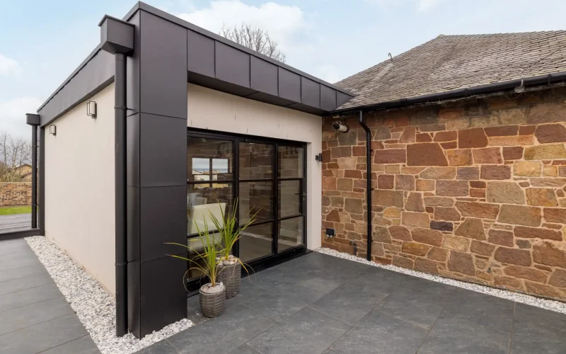 Contemporary house extension featuring black cladding and large glass doors, complementing classic brick walls.